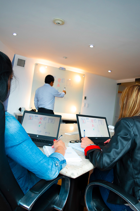 Instructor de SAC-WALABI anotando en un pizarrón mientras dos personas lo observan, representando el servicio de capacitación tecnológica.